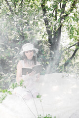 Fototapeta na wymiar Tender girl in a white dress in the flowers of bird cherry
