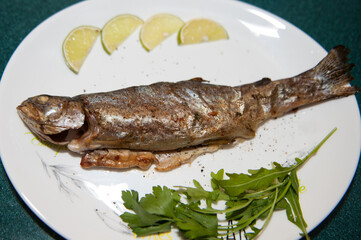 Fried river trout fish on white  plate with lemon and herb
