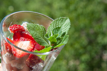 Sweet strawberry with mint in clear glass on green background