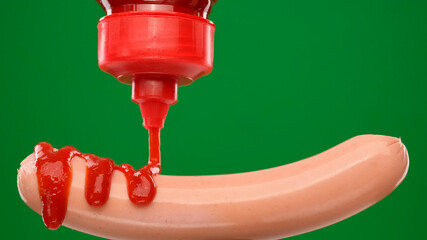 sausage. pouring tomato sauce ketchup on hot sausage. sausage on green background