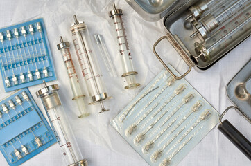 vintage old medical glass syringes and needles on white linen fabric with metal boxes