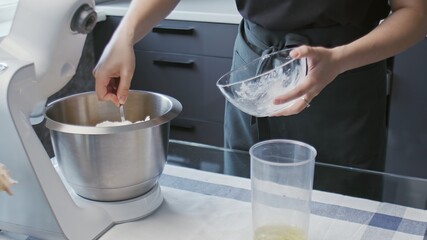 Cooking cake at home. Young attractive housewife poures puts white cream in big mixer