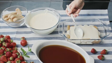 Cooking tiramisu cake at home. Young attractive housewife pours white cream on tiramisu
