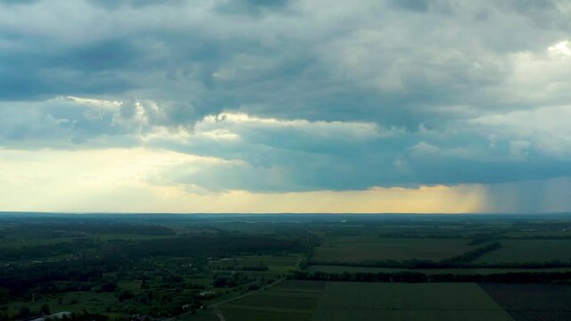Aerial flying above stunning field under dramatic rain cloud rolling. Global warming effect black thunderstorm dramatic rain clouds Dramatic sky. Light rays shining through clouds.        