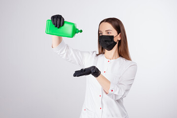 girl in  black mask and gloves pours transparent liquid from  green can, disinfectant solution is poured onto the glove, light gray background