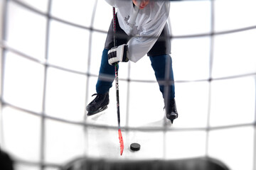 Unrecognizable male hockey player with the stick on ice court and white background. Sportsman wearing equipment and helmet practicing. Concept of sport, healthy lifestyle, motion, action. Close up.
