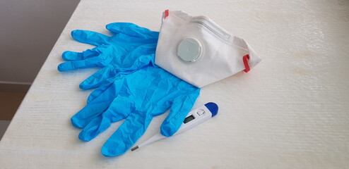 face protection medical mask lay on two blue nitrile gloves near a thermometer