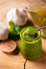 Pesto sauce. In a transparent glass with the ingredients in the background. Olive oil, garlic and basil.