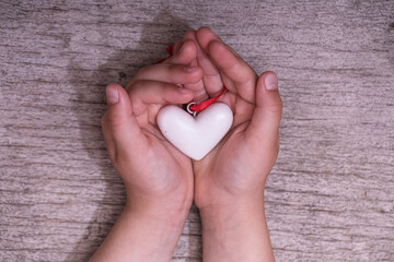 Close up white heart in child hands on old wooden table in vintage retro style. World humanitarian day concept.