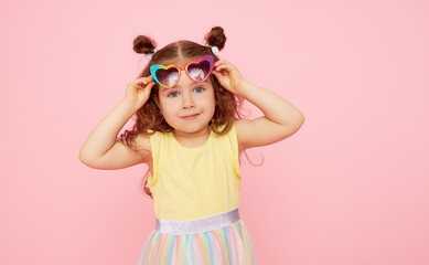 Portrait of surprised cute little toddler girl  in sunglasses over pink background.  Child model...