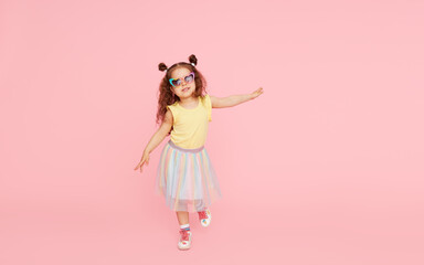 Portrait of surprised cute little toddler girl  in sunglasses over pink background.  Child model have fun and jump. Advertising childrens products