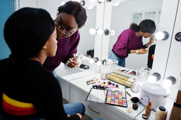Obraz premium African American woman applying make-up by make-up artist at beauty saloon.