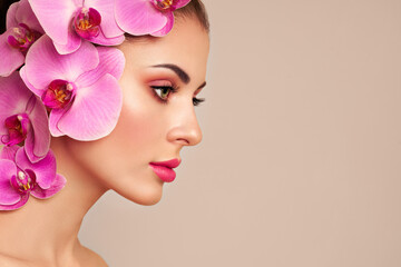 Naklejka premium Portrait of beautiful young woman with orchid. Brunette woman with luxury makeup. Perfect skin. Eyelashes. Cosmetic eyeshadow. Purple flowers