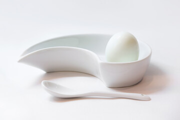 Fototapeta na wymiar White peeled egg on a stand with a ceramic porcelain spoon. White on white. The concept of morning and a perfect Breakfast. Breakfast of an aristocrat