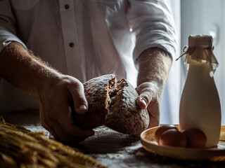Man breaks fresh bread on kitchen table. Food, cooking and baking concept. Ingredients for homemade baking. Organic food