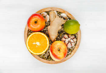 Orange, ginger, garlic, lime, lemon, sunflower seeds, Apple, pumpkin seeds lie on a round wooden plate on a white wooden background. Organic healthy, immune natural products, top view.