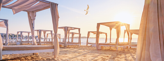 Coastal landscape, banner - view of the sandy seashore with beach gazebos. Beach holiday concept