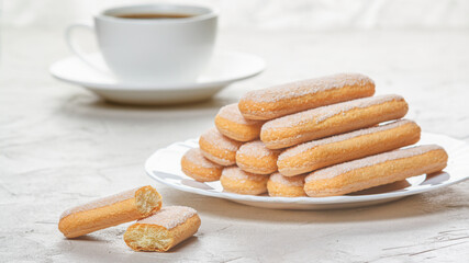 Traditional savoiardi biscuits or ladyfingers cookies on a plate and white cup of coffee on...