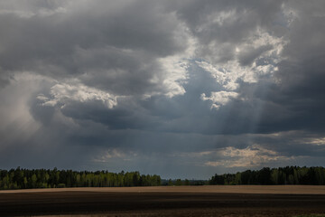 Stormy sky over a sloping field with sunbeams