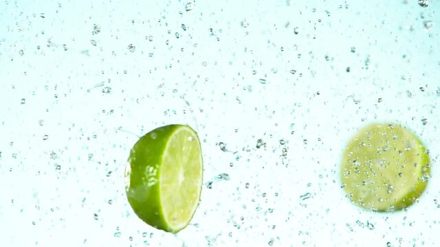 Super slow motion of lime pieces collision with water splashes, white background. Filmed on high speed cinema camera, 1000 fps.