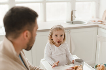 Young cute family with little daughter have breakfast at home in the kitchen.