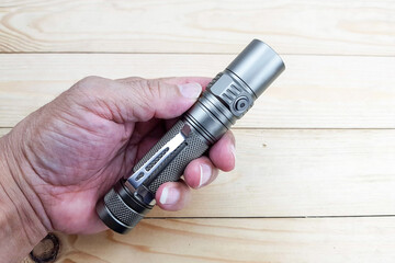 min and high poweri LED flashlight in hand with wood texture background.