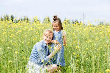 Fototapeta premium Happy family on a summer meadow. little girl child daughter hugging and kissing mother.Yellow field of rapeseed flowers. Freedom is a dream idea.