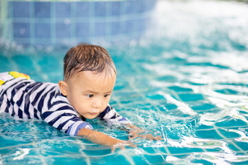 Fototapeta na wymiar Little adorable boy in swimming suit enjoying swimming in the pool