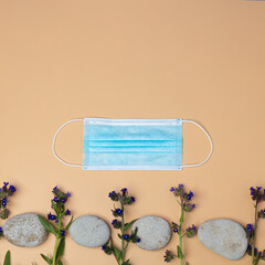 Medical mask, pebbles, flowers
  on an orange background.
Concept: quarantine, on vacation, traveling, take protection from coronavirus
  Style Flat Lay.