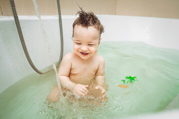 Cute happy little baby boy washing in bathroom with toys, child's hygiene, healthy lifestyle, carefree childhood concept.
