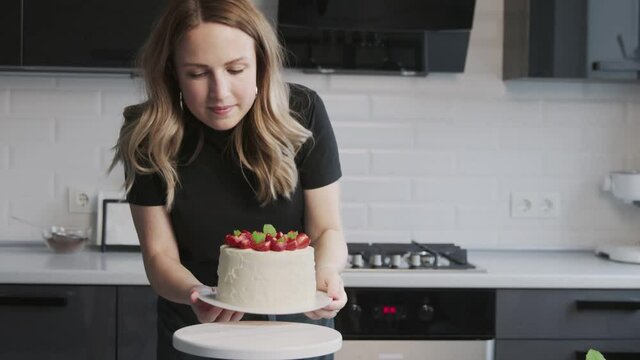 Confectionery blog. Woman in black shirt photographing cake decorated with strawberry.