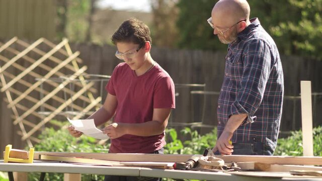 A father and son high five and laugh while working on a DIY construction project in the backyard
