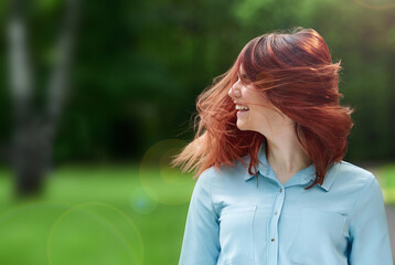 the girl smiles widely, shakes her head with red hair and is happy on the green natural background. happy young bright girl laughing on the summer lawn