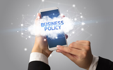 Female hand touching smartphone with BUSINESS POLICY inscription, cloud business concept