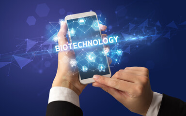 Female hand holding smartphone with BIOTECHNOLOGY inscription, modern technology concept