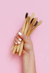 Hand keeps eco friendly bamboo toothbrushes on pink background