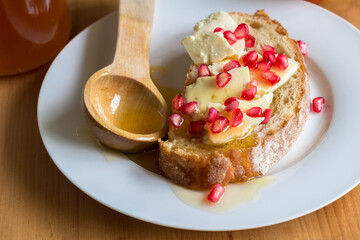 Rustic bread slice with cheese, pomegranate seeds and honey on plate close up