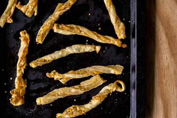 Cheesy cheese pastry straws with sesame seeds and bits of chili in oven pan - top view photo of a tasty delicious snack