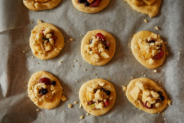 homemade buns with fruit and crumble on white baking paper ready for baking in the oven.