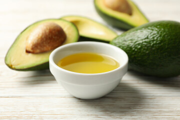 Ripe fresh avocado and oil on white wooden background, close up