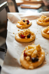 homemade buns with fruit and crumble on white baking paper ready for baking in the oven.