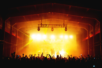 silhouettes of a musical group with bright spotlights on stage and a full hall of a dancing crowd. atmosphere of a music festival. concert poster