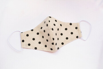 Fashionable protective mask made of white fabric and black polka dots isolated on white background. Covid-19 pandemic protection.