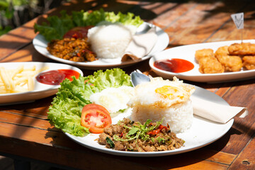 basil stir fry rice with vegetable tomato cucamber salad on white plate and wood table with another food stock photo