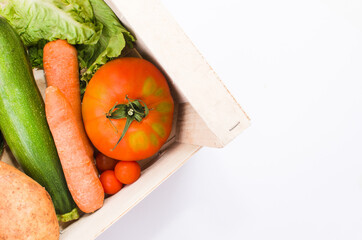 vegetables and greens inside a wooden box. Tomatoes, carrots, zucchini and lettuce. White background