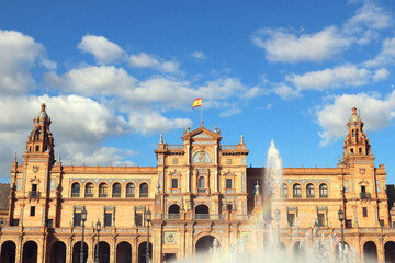 Fototapeta na wymiar plaza de espana seville spain, with the main monument palace, the flag, the fountain and a blue sky with clouds in the background - horizontal postcard or wallpaper