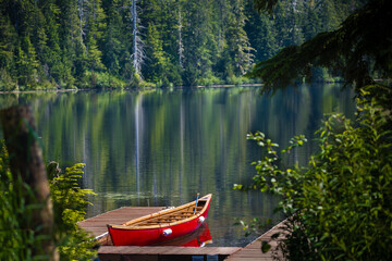 A red canoe docks at the mountain lake in Tongass National Forest  of Alaska. The lake is more than 300 feet deep.  - Powered by Adobe