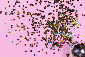 Creative disco cocktail shaped ball cup with flash effect sparkle and splashing out gold colorful confetti on pink background. Concept for holidays and parties. Top view, flat lay, copy space