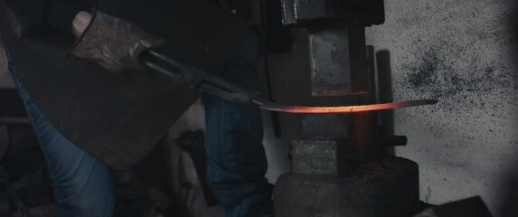 Blacksmith hammering iron with an old machine making knife in dark reopen small business workshop unrecognizable close up