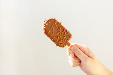 chocolate ice cream with nuts
popsicle on a stick in a man’s hand